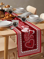 Une belle table de petit déjeuner avec des viennoiseries, de la porcelaine blanche et un chemin de table orné de motifs de cœurs rouges.