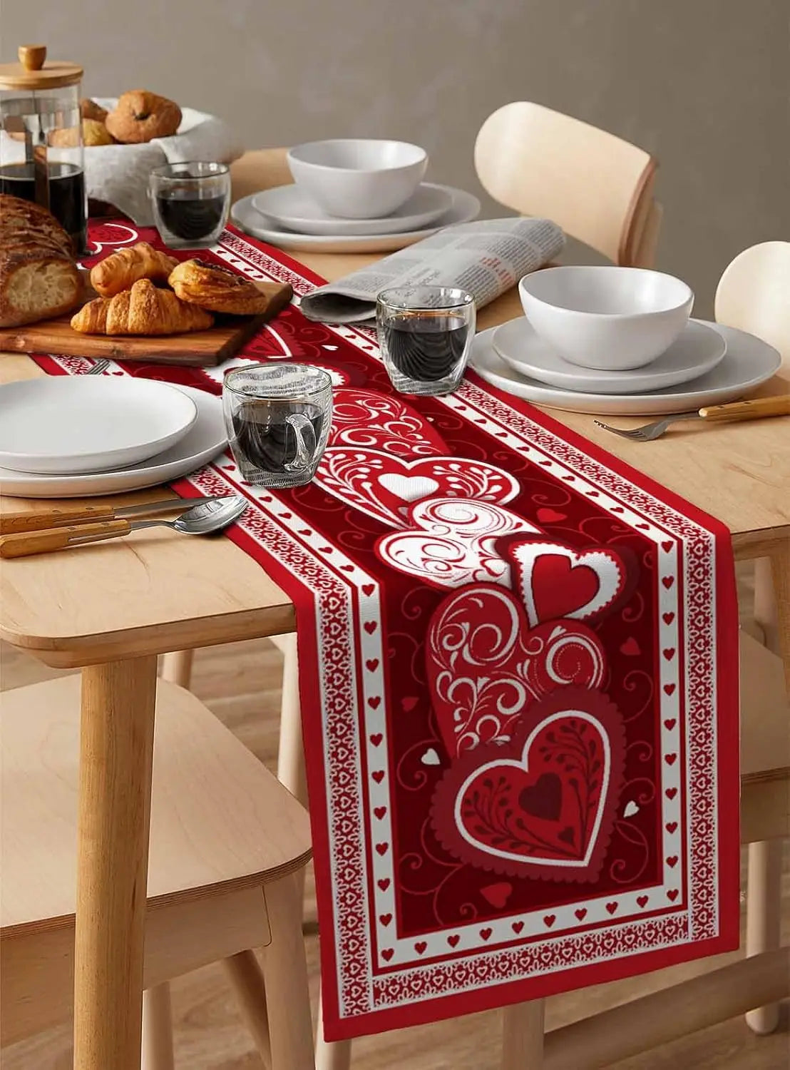Une belle table de petit déjeuner avec des viennoiseries, de la porcelaine blanche et un chemin de table orné de motifs de cœurs rouges.