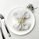 Une serviette blanche élégamment enroulée et attachée avec des anneaux dorés sur une assiette blanche, accompagnée d'un décor floral.