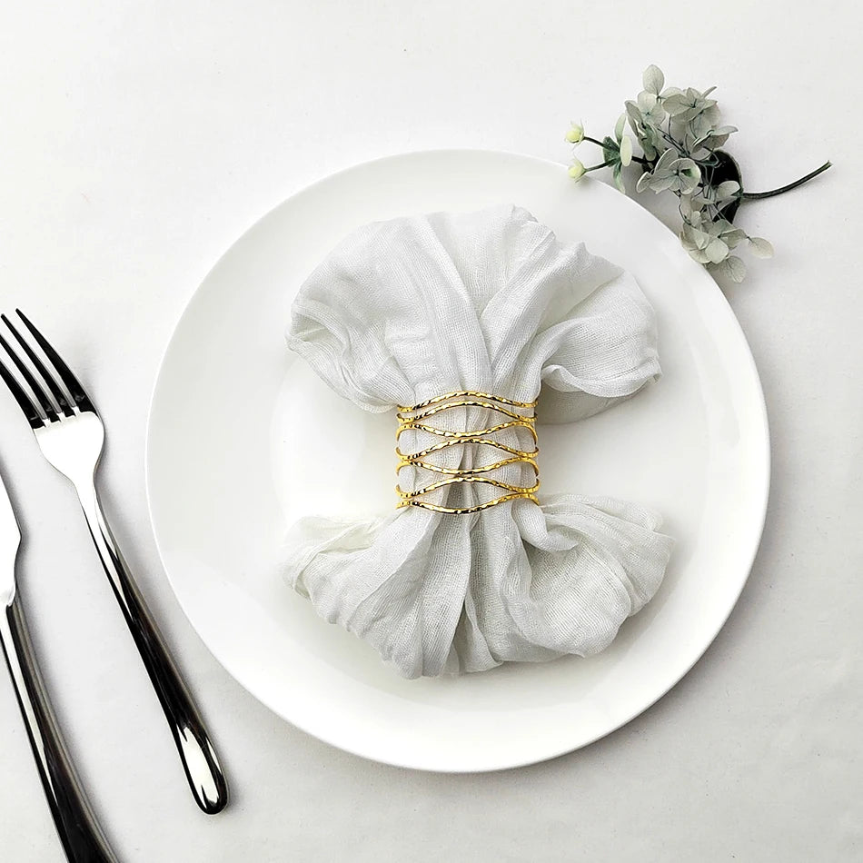 Une serviette blanche élégamment enroulée et attachée avec des anneaux dorés sur une assiette blanche, accompagnée d'un décor floral.