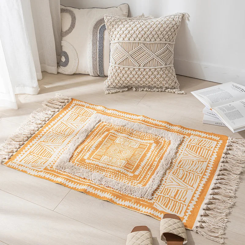 Un tapis décoratif aux motifs ethniques colorés, orné de franges, posé sur le sol d'une pièce lumineuse avec des coussins ornementaux.