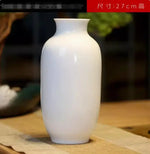 Vase en céramique blanc élégant et minimaliste, posé sur une surface en bois.