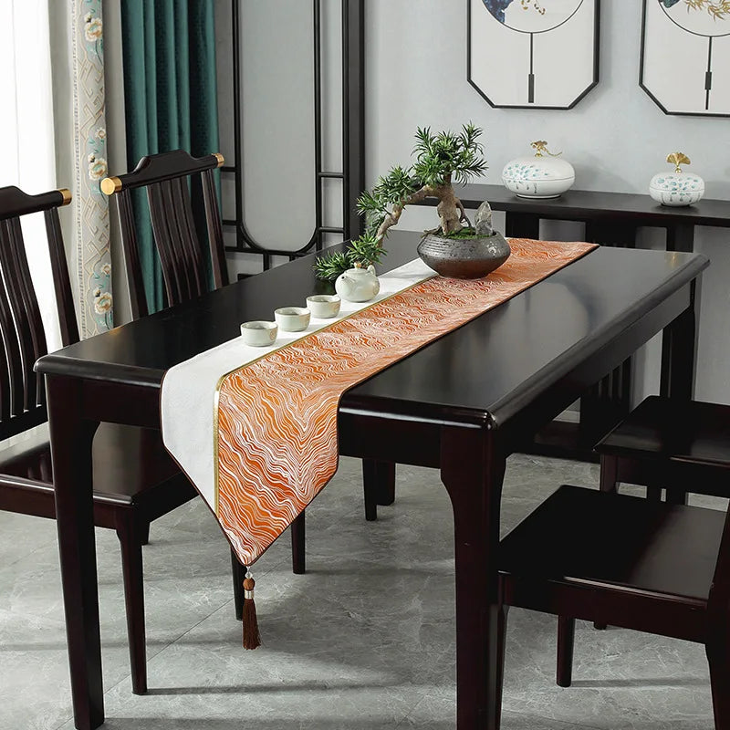 Table à dîner noire élégante avec chemin de table en motif vague orange, décorations végétales et céramiques posées sur la table.