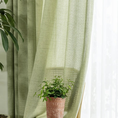 Rideau vert amande translucide laissant passer la lumière, décoré avec une plante dans un pot en terre cuite.