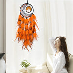 L'image montre un rêve capteur décoratif avec des plumes orange accrochées au mur, derrière une jeune femme assise sur un canapé blanc dans un intérieur lumineux.