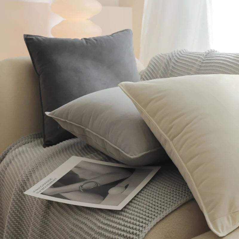 Coussins gris et blanc sur un lit avec une lampe et un magazine posés à côté.