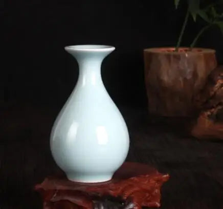Un vase blanc élégant posé sur un fond sombre, avec des fleurs rouges à l'arrière-plan.