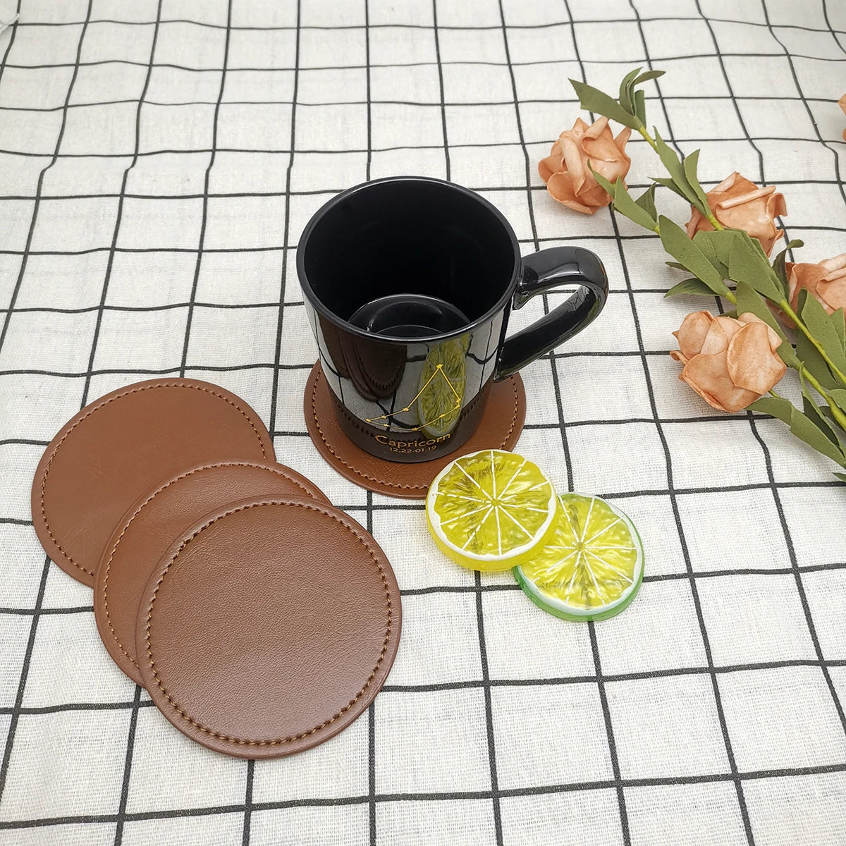 Un ensemble de sous-verres en cuir marron entourant une tasse de café noire avec un motif floral et des tranches de citron vert.