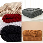 Couvertures tricotées dans différents tons de beige, gris et marron, affichant une texture chaude et douillette, parfaites pour se réchauffer et ajouter une touche confortable à l'intérieur.