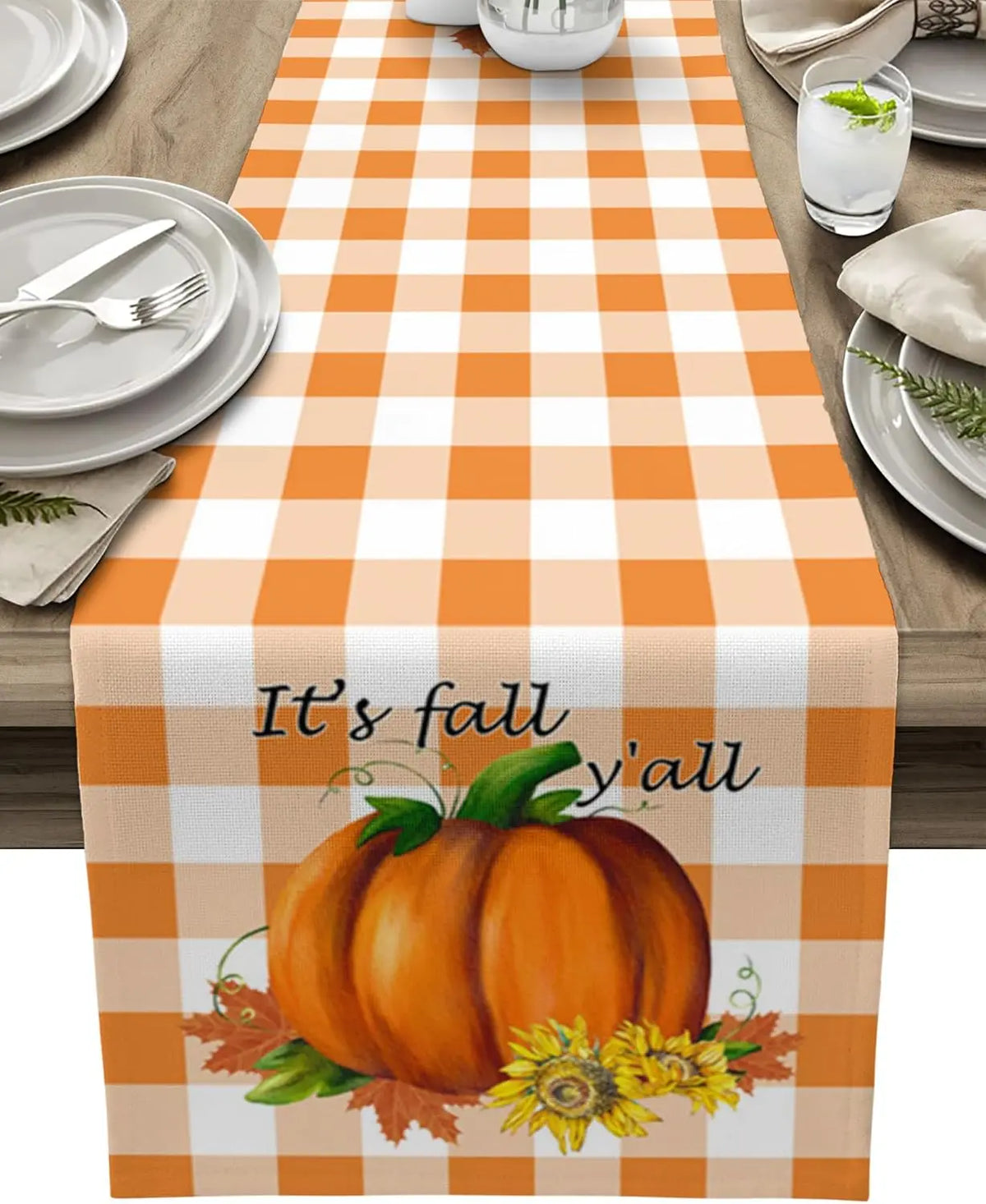 Le centre de la table présente une nappe à motifs carreaux blancs et oranges, avec une grande citrouille orange et des fleurs jaunes, accompagnée de l'inscription "It's fall y'all".