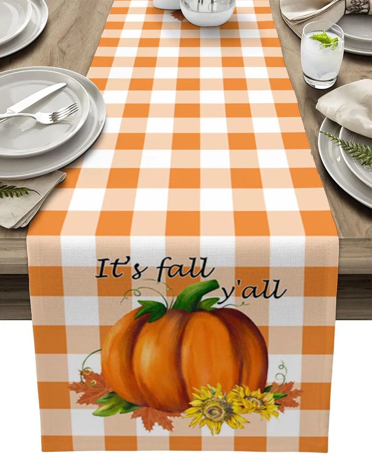 Le centre de la table présente une nappe à motifs carreaux blancs et oranges, avec une grande citrouille orange et des fleurs jaunes, accompagnée de l'inscription "It's fall y'all".