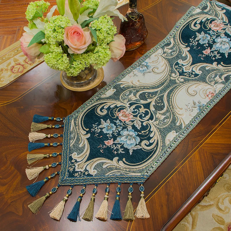Un magnifique bouquet de fleurs colorées posé sur une table de bois, avec une superbe nappe ornée de motifs floraux et de pompons décoratifs.