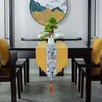 Cette image montre une table à manger dans un intérieur moderne et épuré, avec un chemin de table jaune vif et un superbe décor asiatique comprenant un bonsaï, des vases et une œuvre d'art murale représentant des montagnes brumeuses.