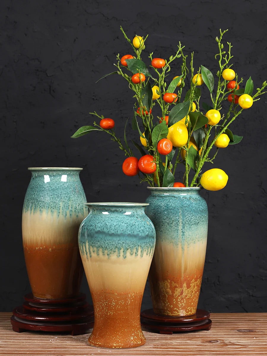 Trois magnifiques vases en céramique aux nuances de vert et d'orange renfermant un bouquet de fruits rouges et jaunes, créant une composition naturelle et élégante.