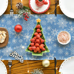 Une table de Noël joliment décorée avec des fraises en forme d'arbre de Noël, des boules de Noël rouges, des flocons de neige et des ustensiles en métal sur un fond en bois avec un motif de flocons de neige.