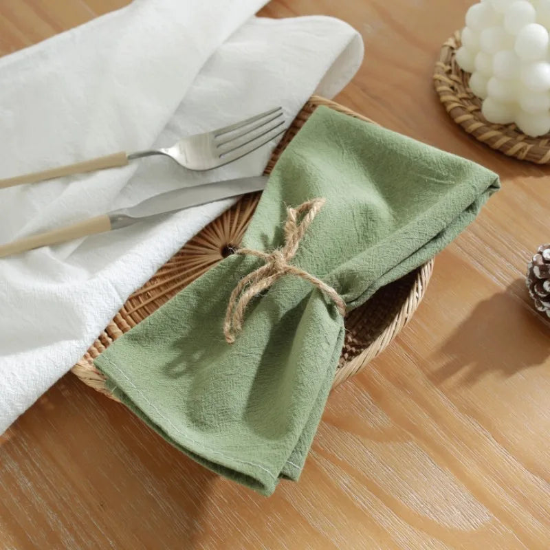 Une serviette de table verte enroulée et attachée avec de la ficelle, placée sur une table en bois avec des ustensiles.