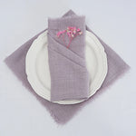 Assiette blanche avec serviette de table grise et fleurs décoratives sur un fond blanc.