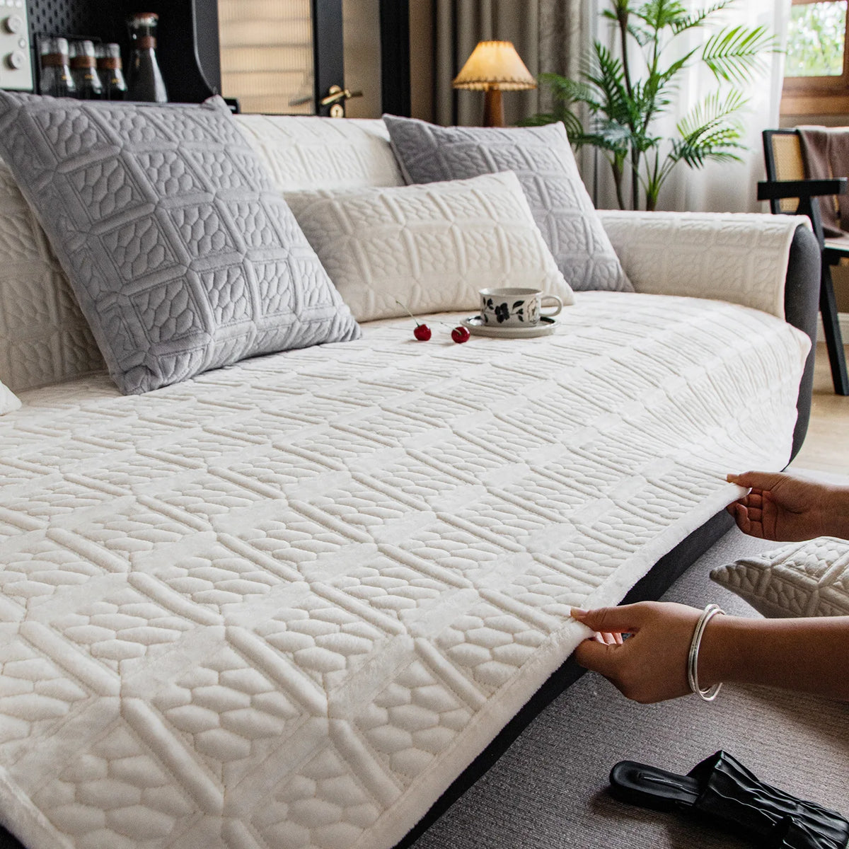 Intérieur de chambre confortable avec un canapé gris capitonné, des coussins moelleux et une tasse de café posée sur la couverture blanche.