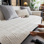 Intérieur de chambre confortable avec un canapé gris capitonné, des coussins moelleux et une tasse de café posée sur la couverture blanche.