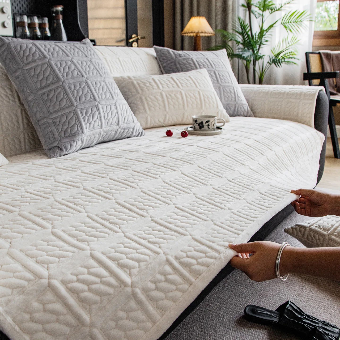 Intérieur de chambre confortable avec un canapé gris capitonné, des coussins moelleux et une tasse de café posée sur la couverture blanche.