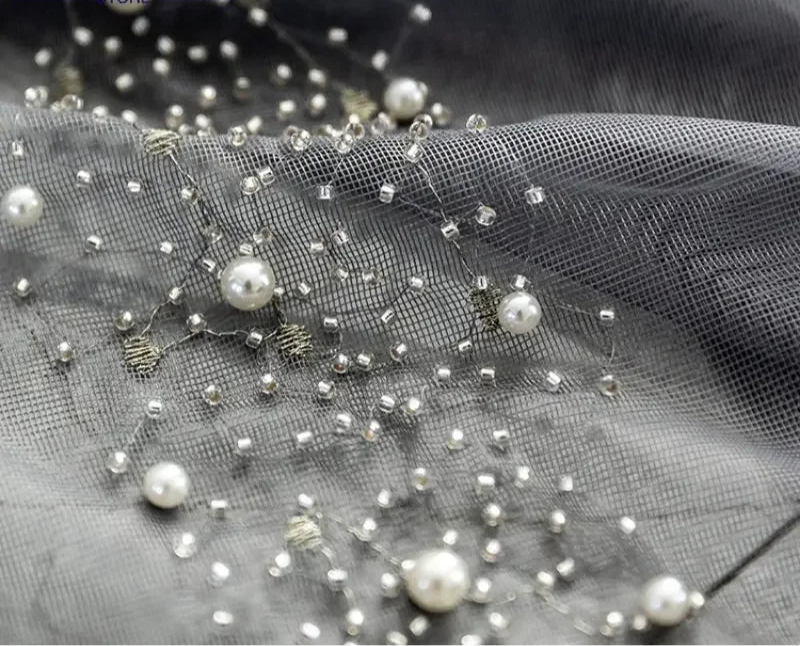 Zoom sur tissu en voile gris perle orné de perles et broderies brillantes.