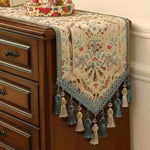 Élégant chemin de table finement décoré de motifs floraux colorés avec des glands et des pompons décoratifs sur les bords.