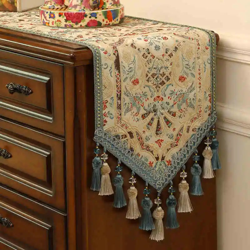 Élégant chemin de table finement décoré de motifs floraux colorés avec des glands et des pompons décoratifs sur les bords.