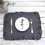 Une scène élégante sur une table en bois avec une assiette blanche ornée de feuilles vertes, accompagnée de couverts dorés sur un fond gris foncé.