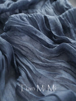 Tissu gris foncé plissé avec l'inscription "Tian Mi Mi" en lettre blanche.