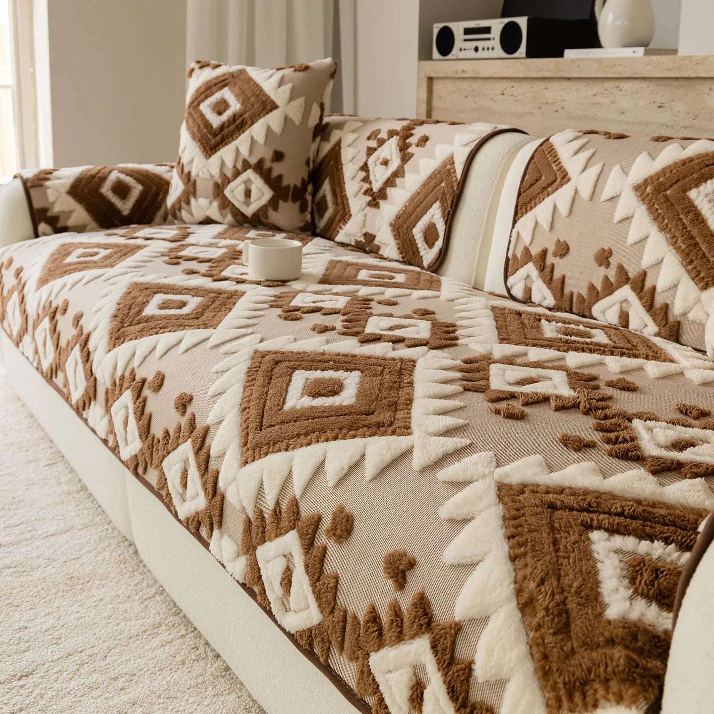 Cette image montre un canapé recouvert d'un motif géométrique ethnique dans des tons beiges et bruns, créant une ambiance chaleureuse et cocooning dans le salon.