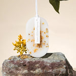 Une bougie décorative ronde blanche et or, sur un socle en pierre brute, avec une fleur jaune sur le côté.