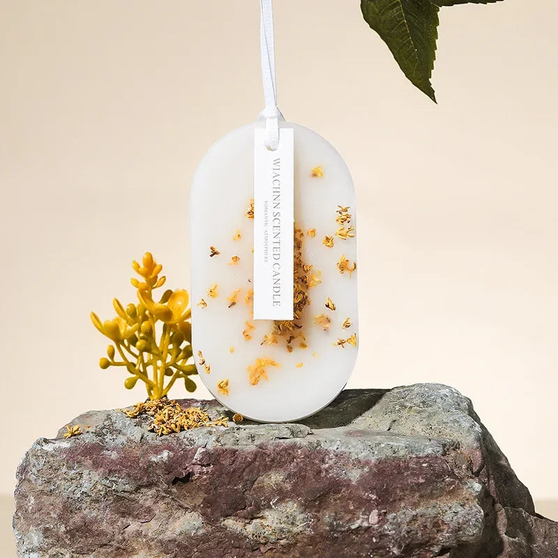 Une bougie décorative ronde blanche et or, sur un socle en pierre brute, avec une fleur jaune sur le côté.