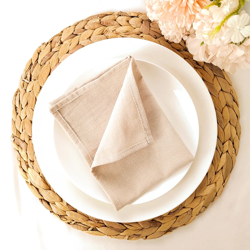 Décor de table élégant avec assiette blanche, serviette beige et napperon en tressage de paille beige, accompagné de fleurs aux tons pastel.