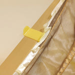 L'image montre une fermeture éclair dorée avec un curseur jaune sur un tissu beige.