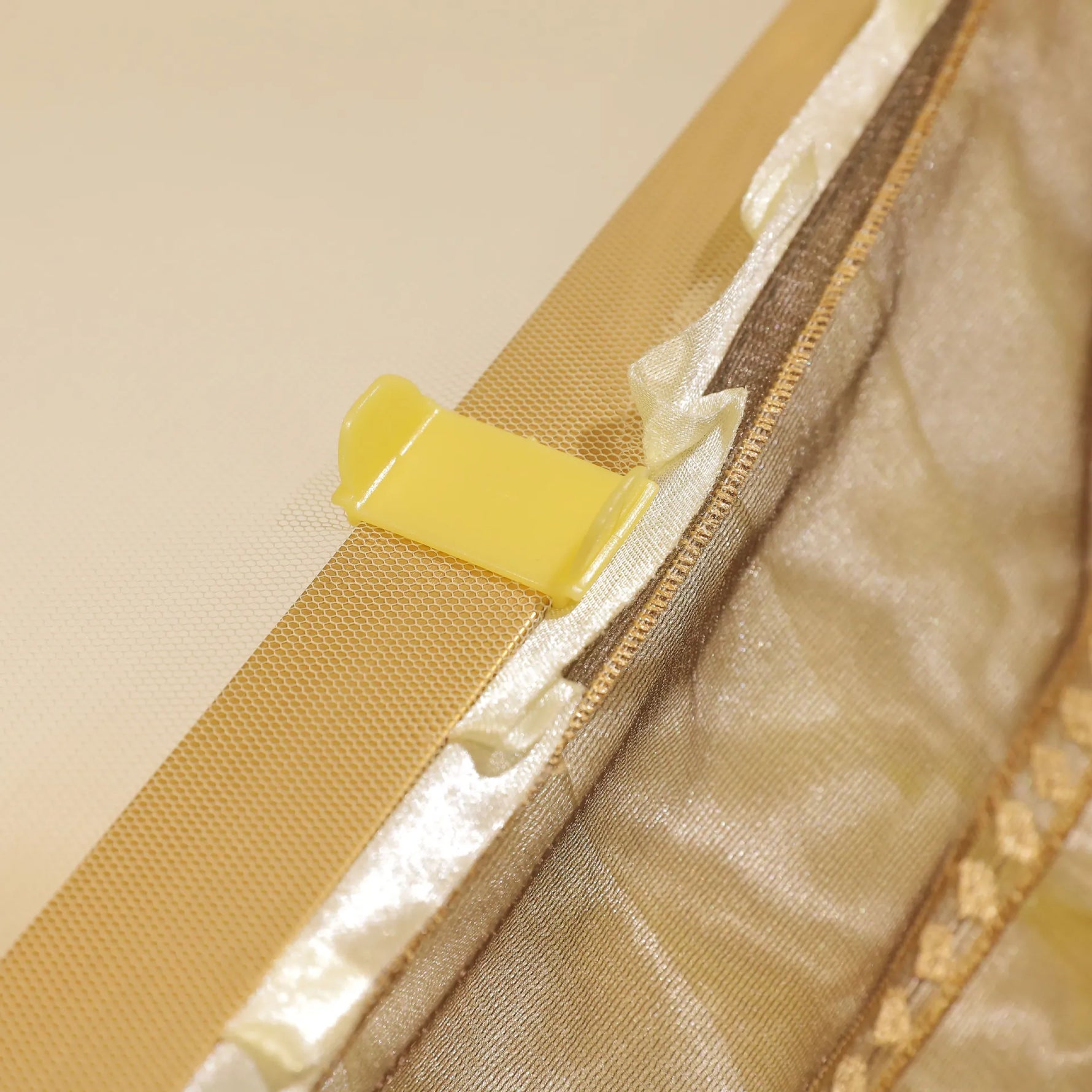 L'image montre une fermeture éclair dorée avec un curseur jaune sur un tissu beige.