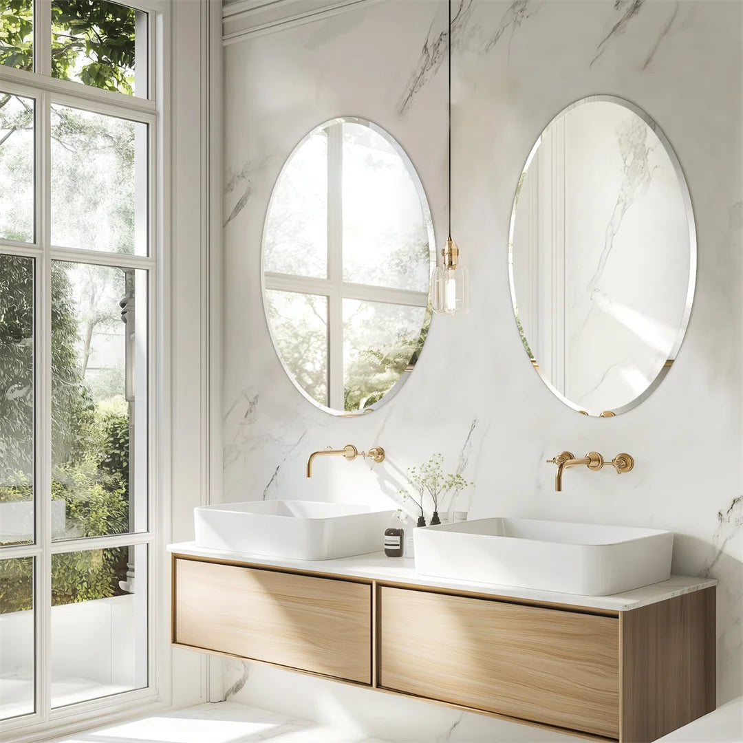 Cette image présente un intérieur de salle de bain élégant et lumineux, avec des miroirs ovales, un plan de travail en bois clair et des appareils sanitaires blancs. Les fenêtres laissent entrer la lumière naturelle, créant une atmosphère sereine et aérée.