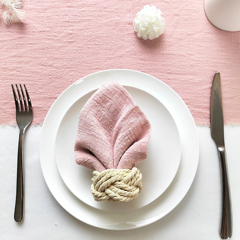Une belle mise en place avec une serviette en textile rose et une décoration végétale, sur une table blanche.