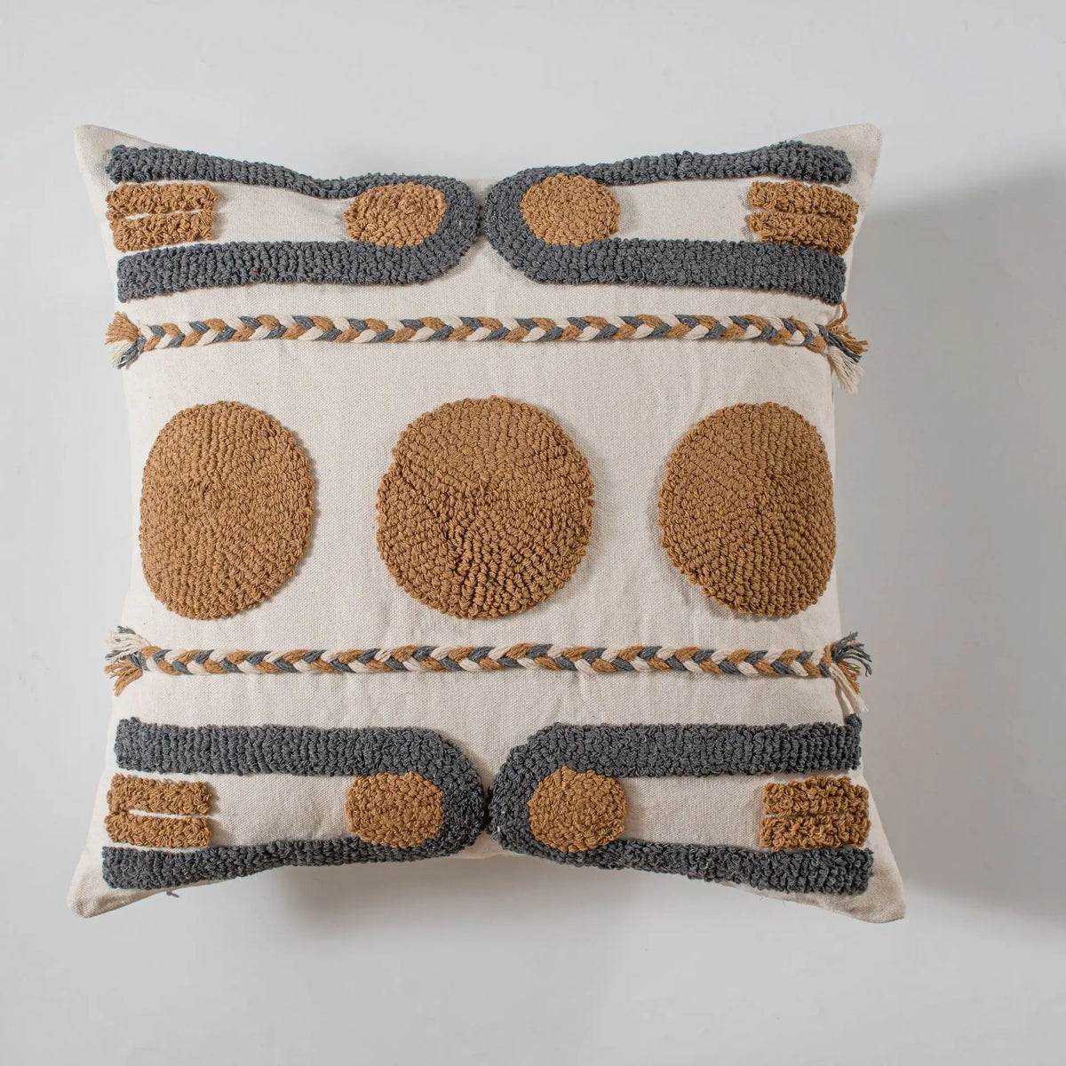 Coussin décoratif crème et beige avec des motifs géométriques texturés et des ornements en macramé, offrant un aspect artisanal et authentique.