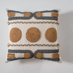 Coussin décoratif crème et beige avec des motifs géométriques texturés et des ornements en macramé, offrant un aspect artisanal et authentique.