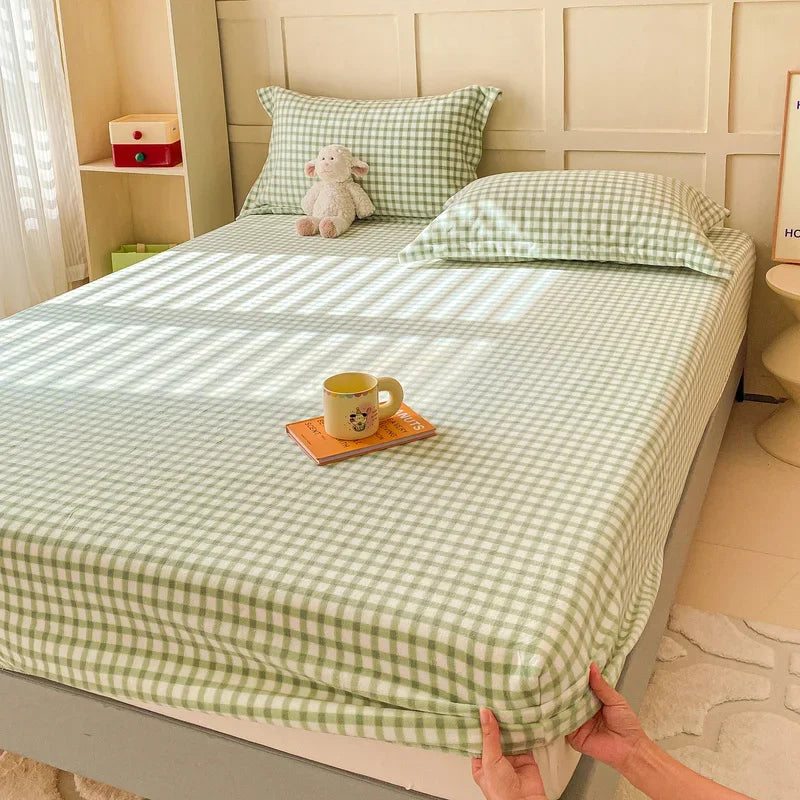 Lit double avec une literie aux motifs de carreaux verts et blancs, ainsi qu'une peluche et une tasse sur le dessus.