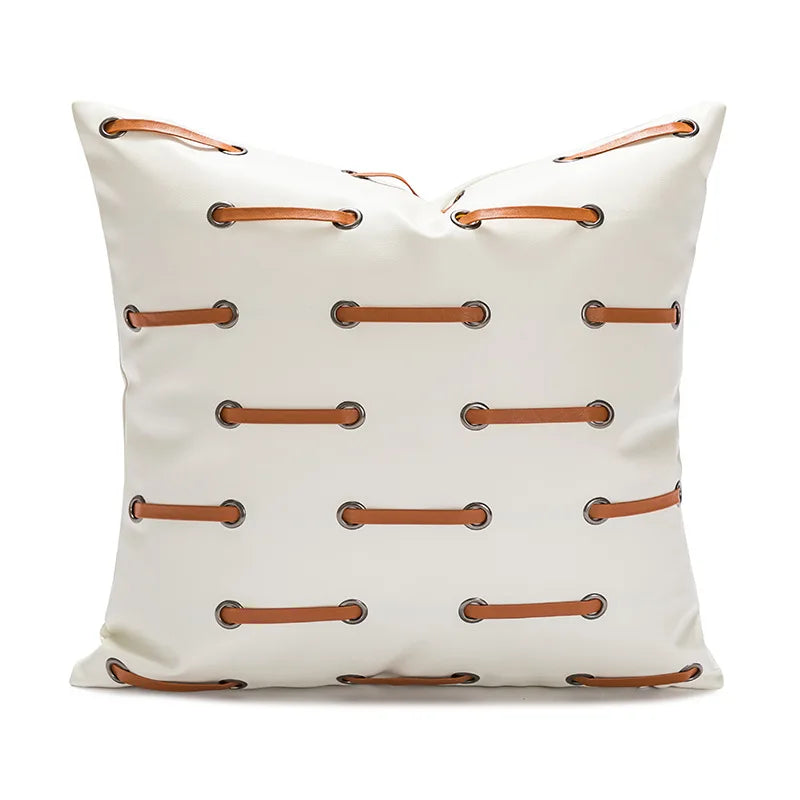 Coussin en cuir blanc avec des attaches en métal marron, créant un motif symétrique sur la surface.