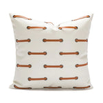 Coussin en cuir blanc avec des attaches en métal marron, créant un motif symétrique sur la surface.