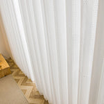 Rideaux en voile blanc brodé installés sur une grande baie vitrée, intérieur lumineux et naturel.