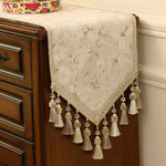 Élégant chemin de table en dentelle blanche avec des pompons, posé sur un meuble vintage en bois, apportant une touche de sophistication à l'environnement.