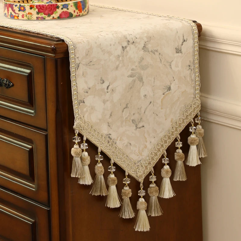 Élégant chemin de table en dentelle blanche avec des pompons, posé sur un meuble vintage en bois, apportant une touche de sophistication à l'environnement.
