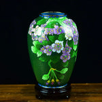 Un vase en émail cloisonné de couleur verte avec des motifs de fleurs de couleur violet et blanc sur un fond sombre.