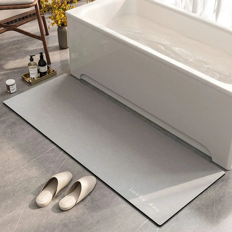 Tapis de bain gris avec des pantoufles blanches sur le sol près d'une baignoire blanche et de quelques éléments de décoration dans une salle de bain moderne.