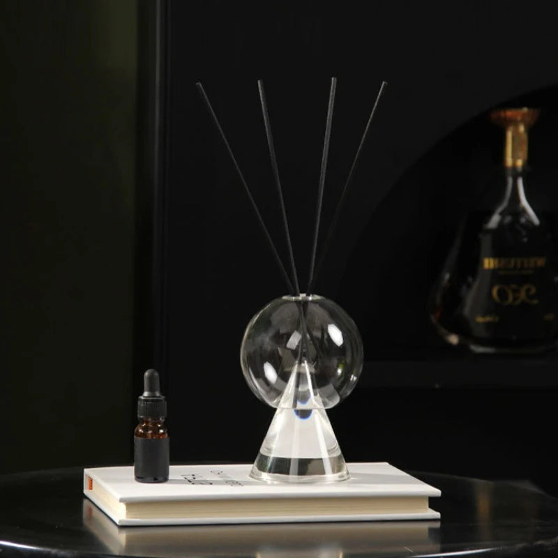 vase verre transparent diffuseur aromates socle triangulaire bâtonnets noirs plante pot blanc livres table