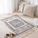 Tapis décoratif en macramé avec motifs géométriques et franges, accompagné de coussins assortis, créant une ambiance chaleureuse et harmonieuse dans cette pièce lumineuse.