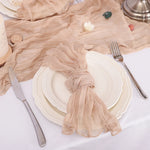 Assiette blanche avec serviette beige chiffonnée sur une table, couverts en métal posés à côté.